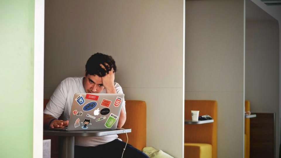 Hombre con estrés laboral sosteniéndose la cabeza frente a su escritorio