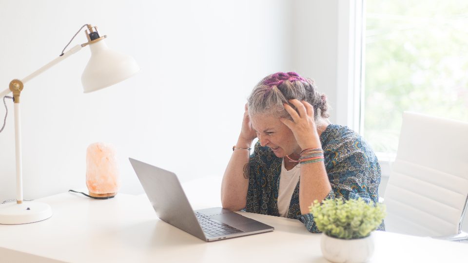 Mujer frente al computador sosteniéndose la cabeza por un dolor de cabeza intenso